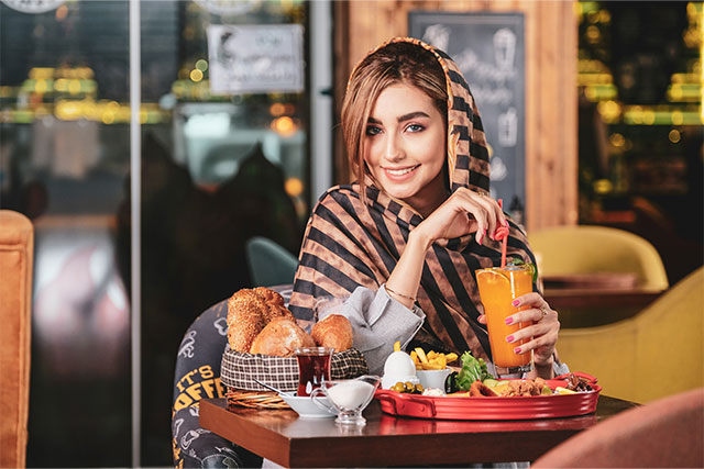 Smiling woman in a cozy restaurant enjoying a fresh vegan meal with a juice.