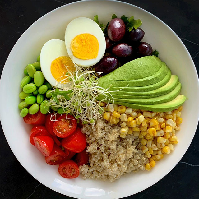 Quinoa power bowl with sliced avocado, cherry tomatoes, corn, green peas, and boiled egg, perfect for a nutritious vegan or vegetarian meal.